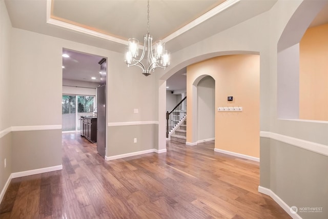 unfurnished dining area featuring hardwood / wood-style floors, a raised ceiling, and a notable chandelier