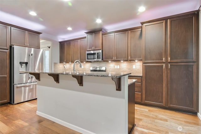 kitchen with light stone counters, appliances with stainless steel finishes, a kitchen island with sink, and a breakfast bar area