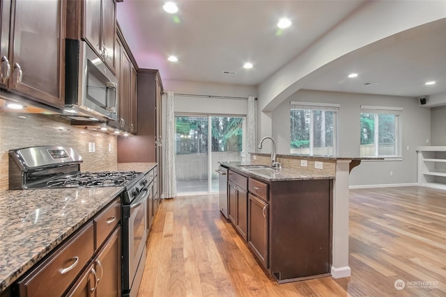 kitchen featuring appliances with stainless steel finishes, light wood-type flooring, stone counters, a breakfast bar, and sink