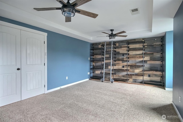 unfurnished bedroom with carpet floors, ceiling fan, wooden walls, and a tray ceiling