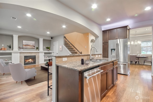 kitchen featuring a kitchen bar, an island with sink, stainless steel appliances, light stone counters, and sink