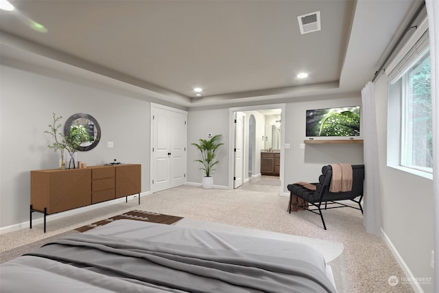 carpeted bedroom featuring a tray ceiling and ensuite bathroom