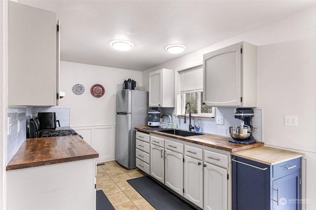 kitchen with white cabinets, stainless steel refrigerator, butcher block counters, and sink