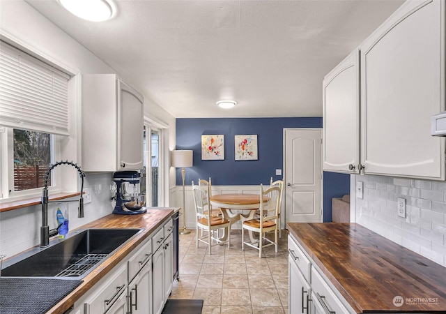 kitchen with butcher block countertops, white cabinetry, sink, and tasteful backsplash