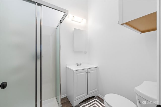 bathroom featuring hardwood / wood-style flooring, vanity, a shower with shower door, and toilet