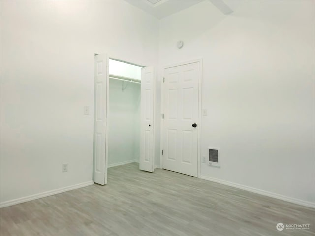 unfurnished bedroom with a high ceiling, light wood-type flooring, and a closet