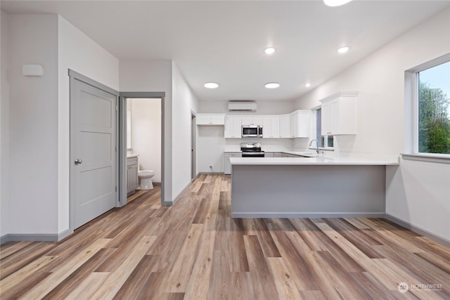 kitchen with kitchen peninsula, appliances with stainless steel finishes, sink, light hardwood / wood-style floors, and white cabinetry