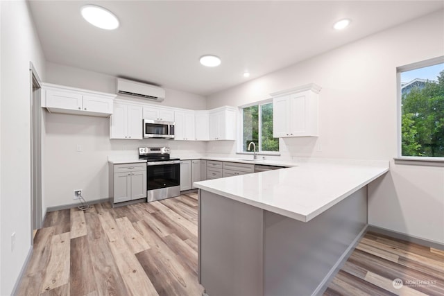 kitchen with sink, a wall mounted AC, appliances with stainless steel finishes, white cabinets, and light wood-type flooring