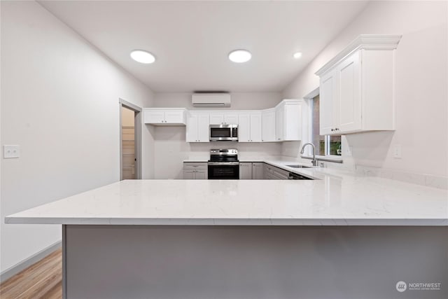 kitchen featuring a wall mounted air conditioner, white cabinets, sink, kitchen peninsula, and stainless steel appliances