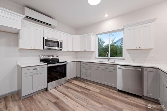 kitchen featuring gray cabinetry, sink, a wall mounted air conditioner, appliances with stainless steel finishes, and light wood-type flooring