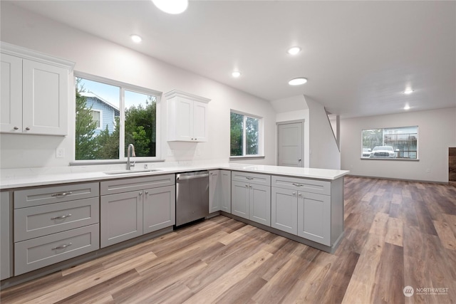 kitchen featuring white cabinets, sink, stainless steel dishwasher, light wood-type flooring, and kitchen peninsula