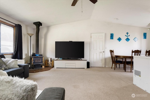 carpeted living room featuring a wood stove, ceiling fan, and vaulted ceiling