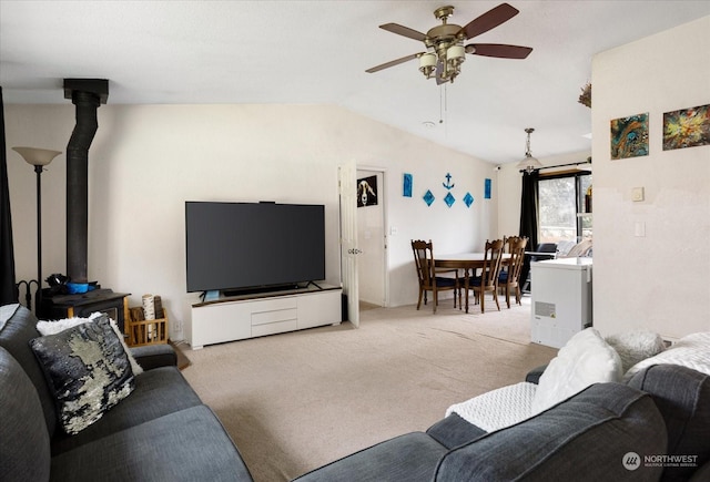 living room featuring vaulted ceiling, light colored carpet, a wood stove, and ceiling fan