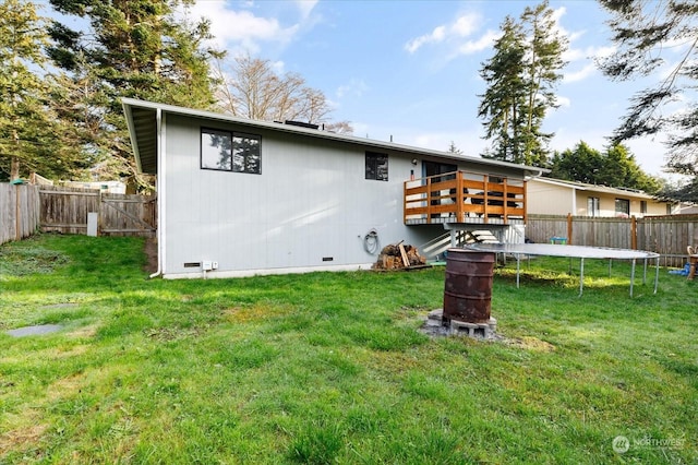 rear view of house featuring a yard, a trampoline, and a wooden deck