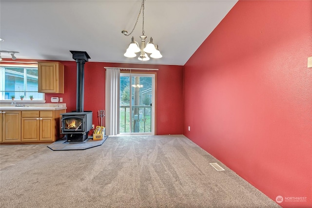 unfurnished living room with an inviting chandelier, light colored carpet, a wood stove, and sink