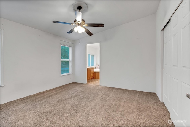 unfurnished bedroom featuring ceiling fan, light colored carpet, connected bathroom, and a closet