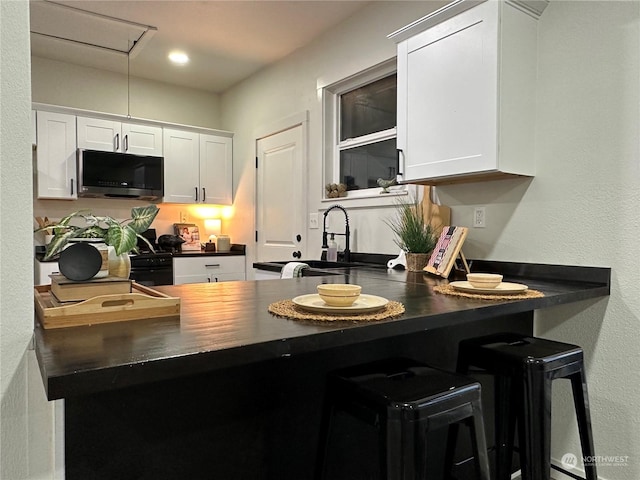 kitchen featuring white cabinets, a kitchen bar, sink, and black range oven