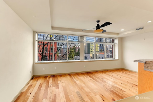 unfurnished living room featuring a raised ceiling, ceiling fan, and light wood-type flooring