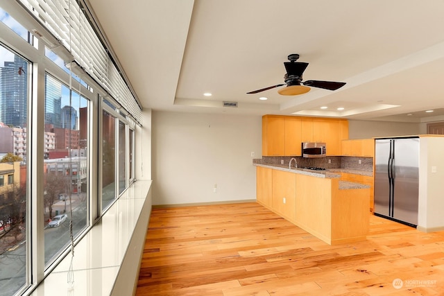 kitchen featuring a raised ceiling, appliances with stainless steel finishes, tasteful backsplash, light hardwood / wood-style floors, and kitchen peninsula