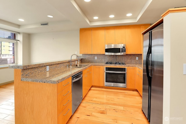 kitchen with sink, stainless steel appliances, kitchen peninsula, light hardwood / wood-style floors, and a tray ceiling