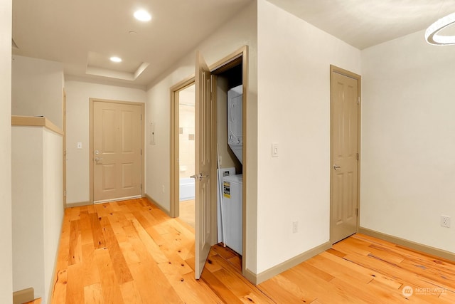 hallway with a raised ceiling, wood-type flooring, and stacked washer / drying machine