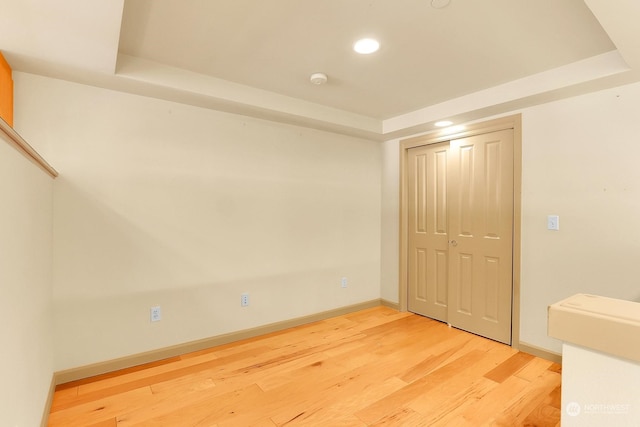 unfurnished bedroom with hardwood / wood-style floors, a tray ceiling, and a closet