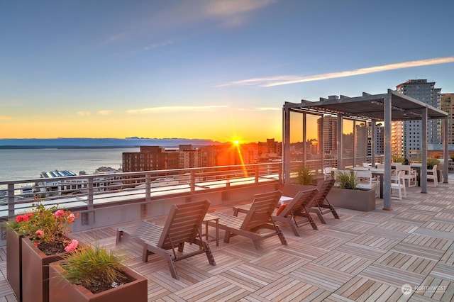 patio terrace at dusk with a pergola, a balcony, and a water view