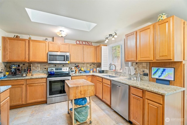 kitchen featuring sink, light stone counters, a skylight, stainless steel appliances, and backsplash