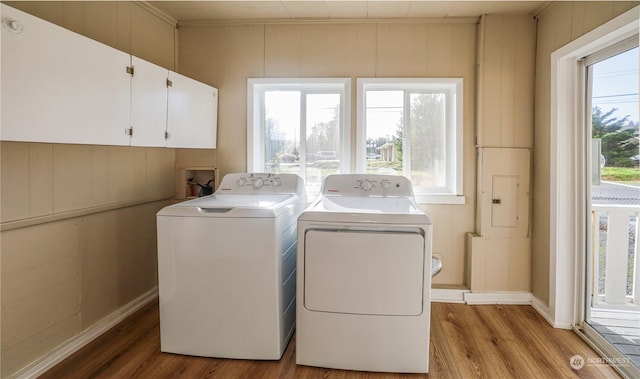 laundry area with cabinets, washer and dryer, wood walls, and light hardwood / wood-style flooring