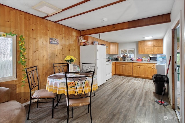 dining room featuring beamed ceiling, wood walls, and light hardwood / wood-style flooring