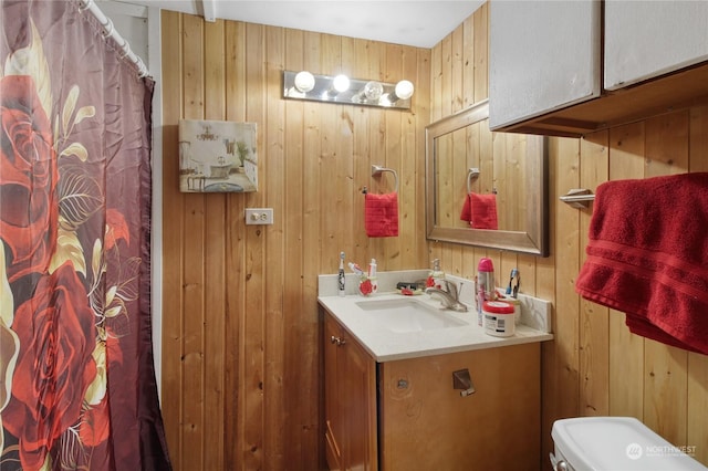 bathroom with vanity, toilet, and wood walls