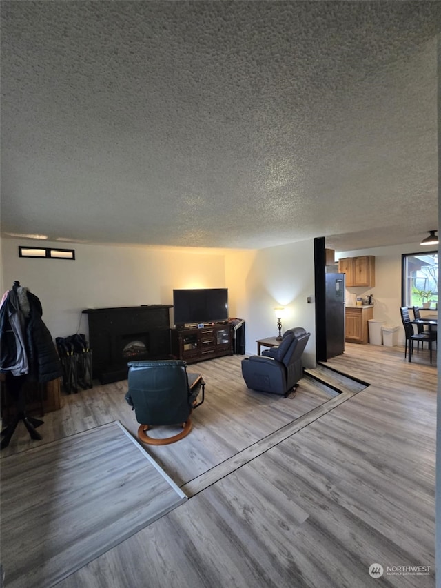 living room featuring a fireplace, ceiling fan, a textured ceiling, and light hardwood / wood-style flooring