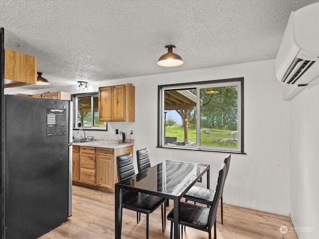 kitchen featuring black refrigerator, light wood-type flooring, an AC wall unit, and plenty of natural light