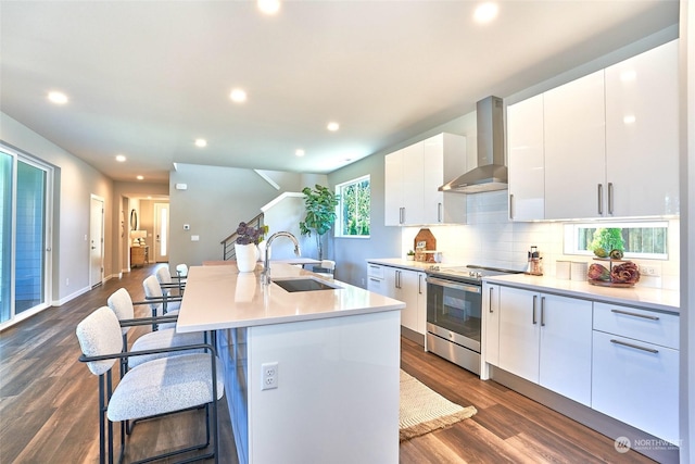 kitchen with electric stove, sink, white cabinetry, a center island with sink, and wall chimney exhaust hood