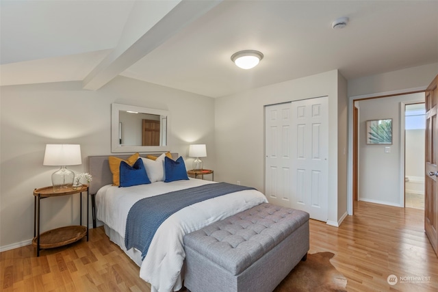 bedroom featuring beamed ceiling, ensuite bath, light wood-type flooring, and a closet