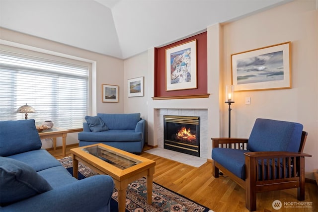 living room with a tiled fireplace, lofted ceiling, and light wood-type flooring