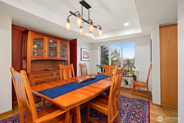 dining room with baseboards, recessed lighting, an inviting chandelier, light wood-style floors, and a raised ceiling