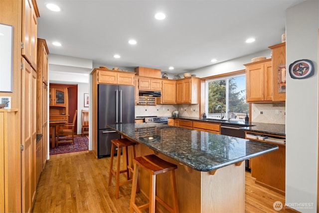 kitchen with light wood-style flooring, under cabinet range hood, recessed lighting, appliances with stainless steel finishes, and a breakfast bar area