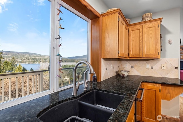 kitchen featuring decorative backsplash, brown cabinets, dark stone counters, and a sink