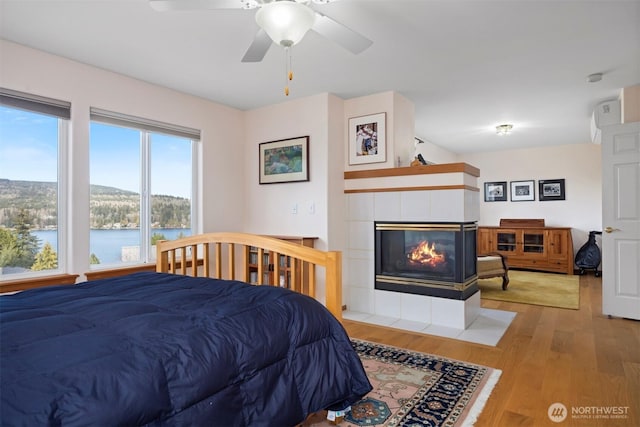 bedroom featuring a water view, wood finished floors, and a tiled fireplace