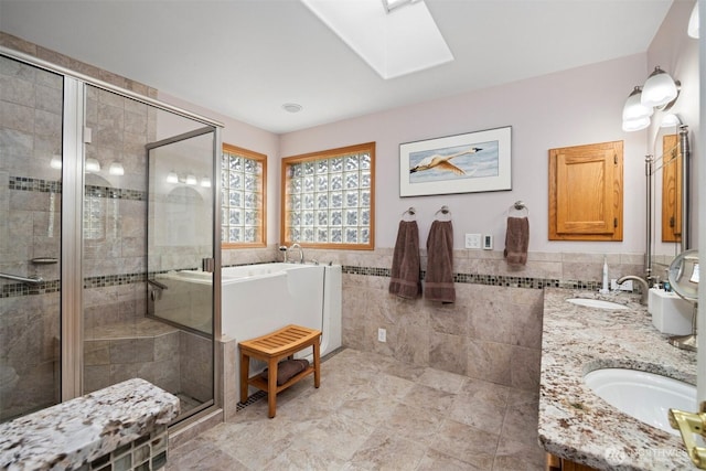 full bath featuring double vanity, a skylight, a stall shower, a sink, and tile walls