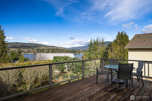 wooden deck with outdoor dining space, a forest view, and a water view