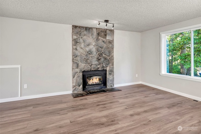 unfurnished living room featuring wood-type flooring, a stone fireplace, a textured ceiling, and rail lighting