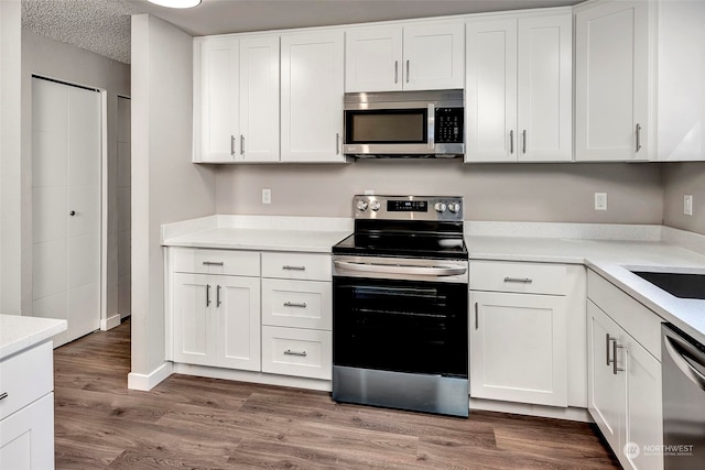 kitchen with white cabinetry, wood-type flooring, stainless steel appliances, and a textured ceiling