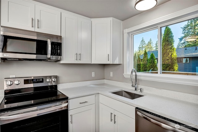 kitchen with stainless steel appliances, white cabinetry, light stone countertops, and sink