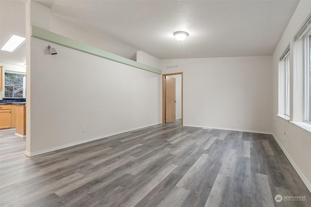 unfurnished room featuring lofted ceiling with skylight, plenty of natural light, a textured ceiling, and dark hardwood / wood-style flooring