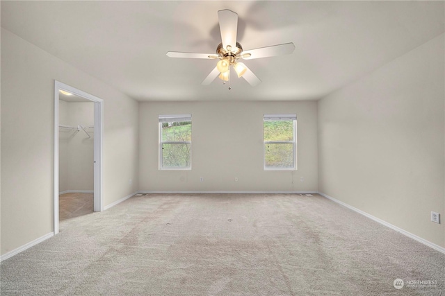 unfurnished bedroom featuring ceiling fan, light colored carpet, a spacious closet, and multiple windows