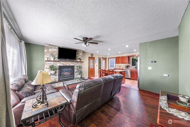 living room with a textured ceiling, hardwood / wood-style flooring, a stone fireplace, and ceiling fan