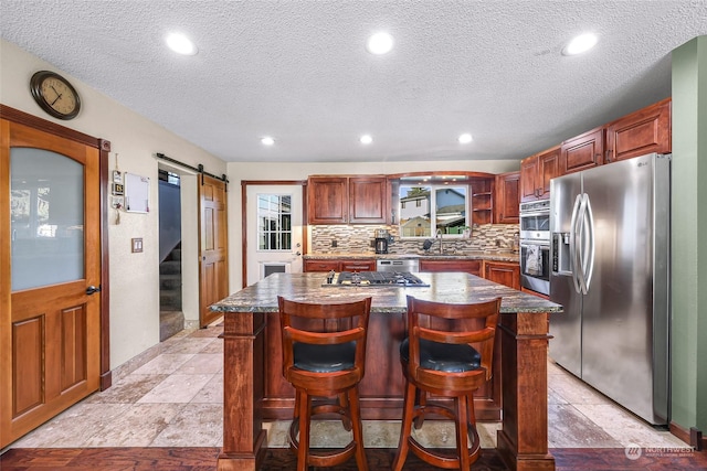 kitchen with stainless steel appliances, a barn door, backsplash, a breakfast bar area, and a kitchen island