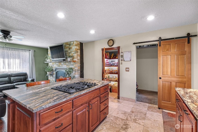 kitchen featuring ceiling fan, a center island, gas stovetop, a stone fireplace, and a textured ceiling